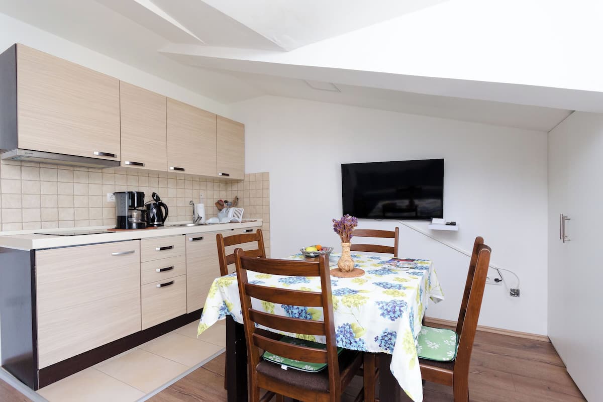 Una cocina compacta con armarios de madera, una mesa de comedor con sillas y un televisor de pantalla plana montado en la pared.