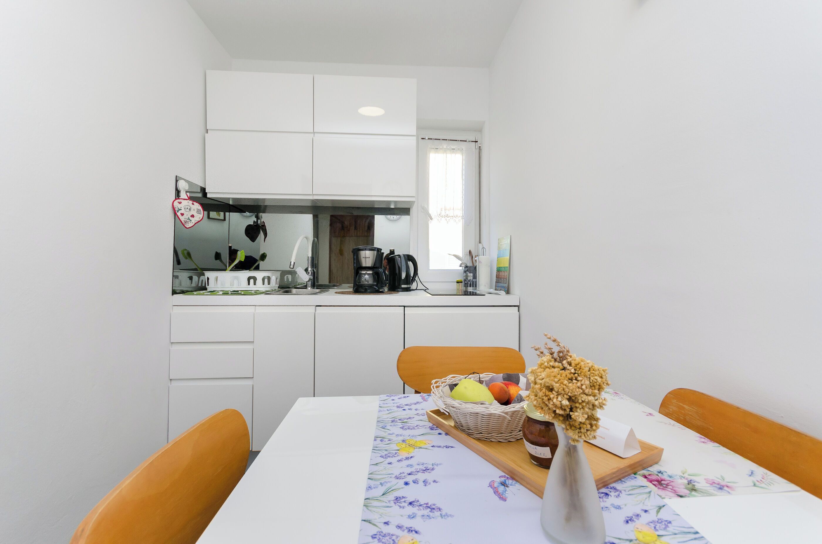 Una cocina compacta con armarios blancos, una cafetera y una cesta de fruta en la encimera.