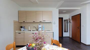 A modern kitchen with wooden cabinets, a dining table with a floral tablecloth, and a vase with flowers.