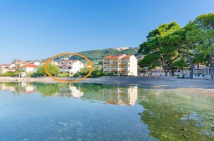 Un hotel frente al agua con aguas cristalinas que reflejan los edificios, una montaña al fondo y un jardín bien cuidado.