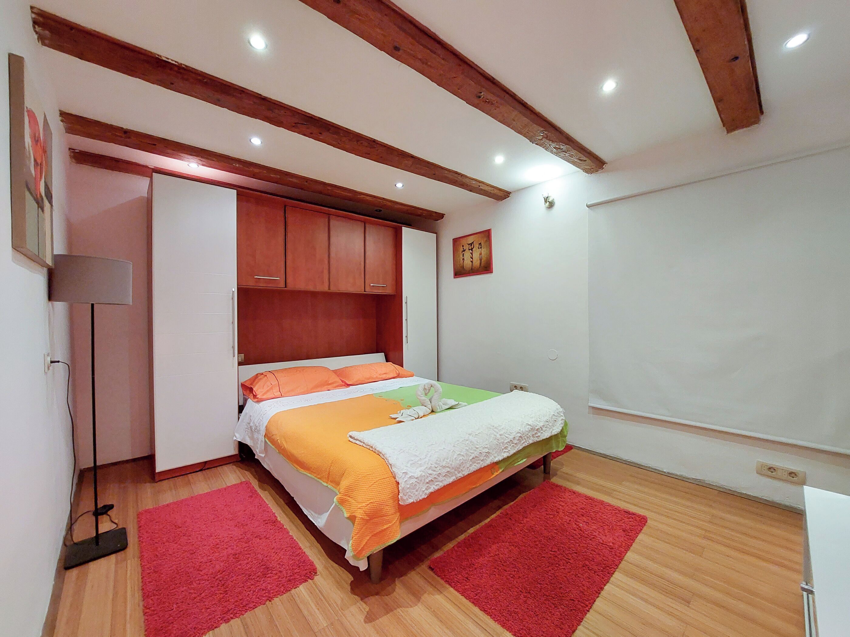 Een slaapkamer met een bed, houten balken, een rood tapijt, een witte muur en een schilderij.