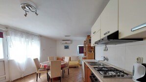A compact kitchen with a gas stove, sink, and a dining area with chairs and a table. - Apartments Ineska (Crikvenica)