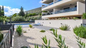 Un edificio moderno con varios balcones que dan a un área ajardinada con piscina y sillones de descanso.