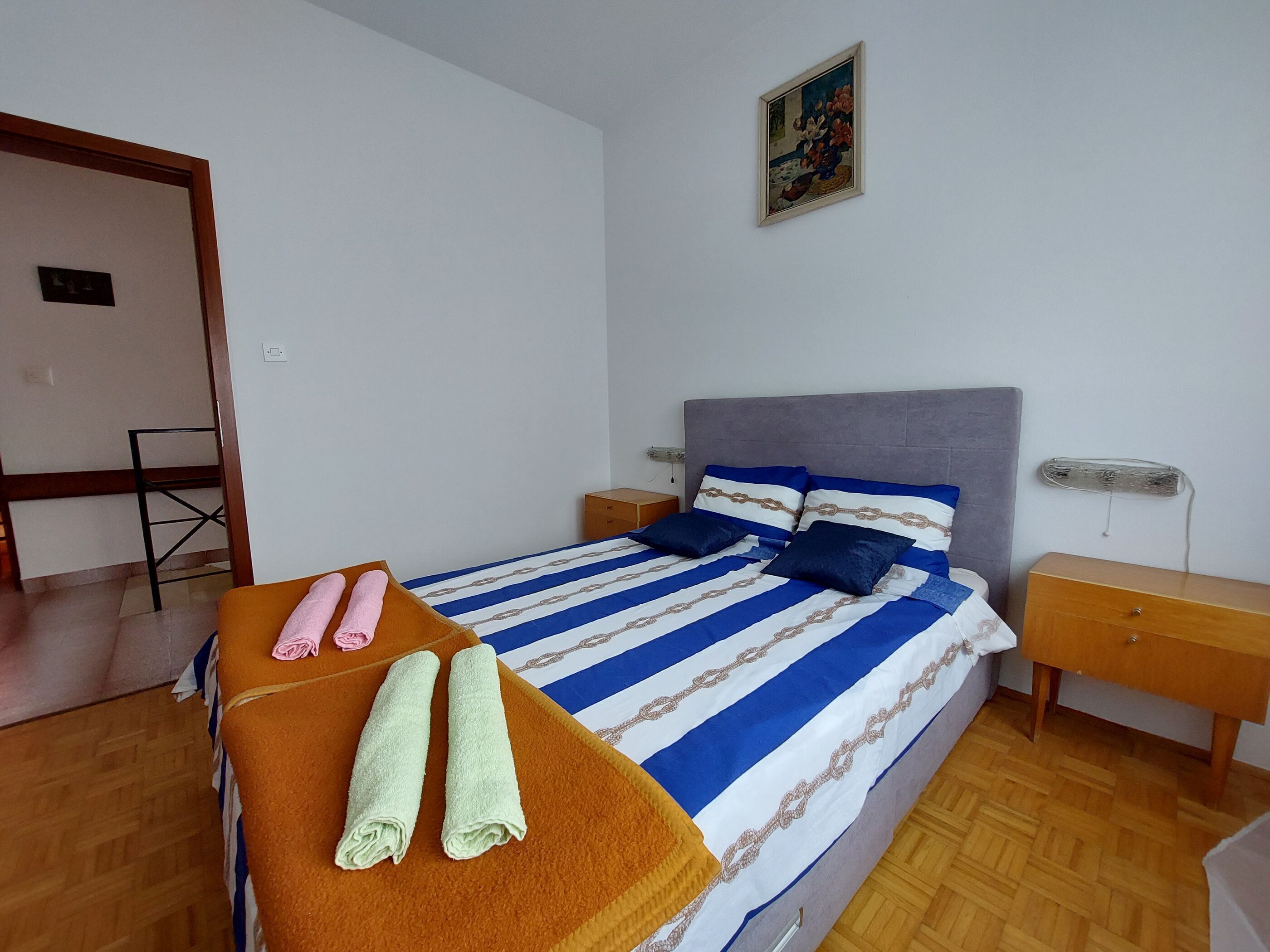 A bedroom with a bed, two nightstands, a wooden floor, and a painting on the wall.