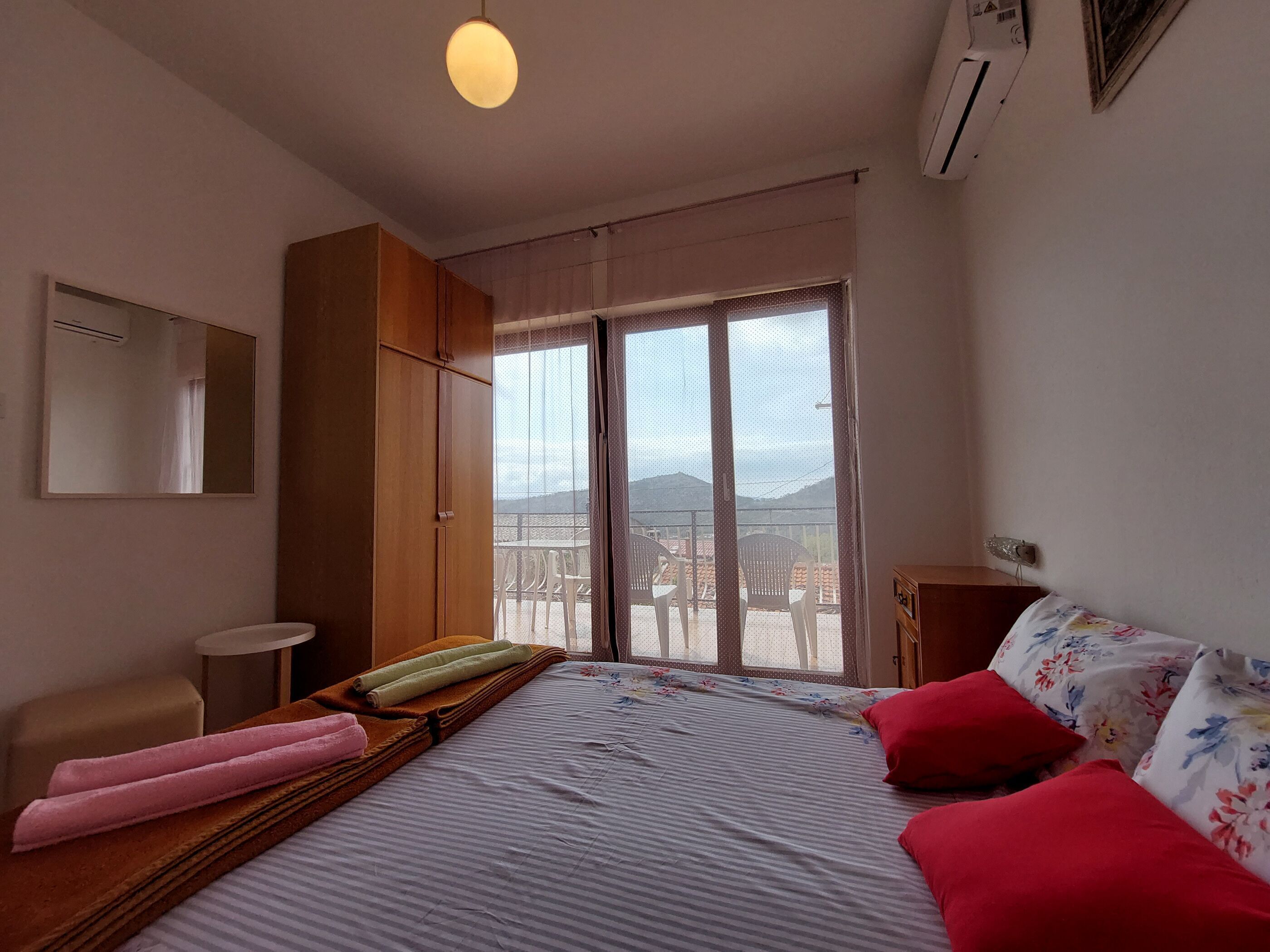 Een hotelkamer met een bed, een klein tafeltje, een stoel, een kledingkast en een balkon met stoelen.