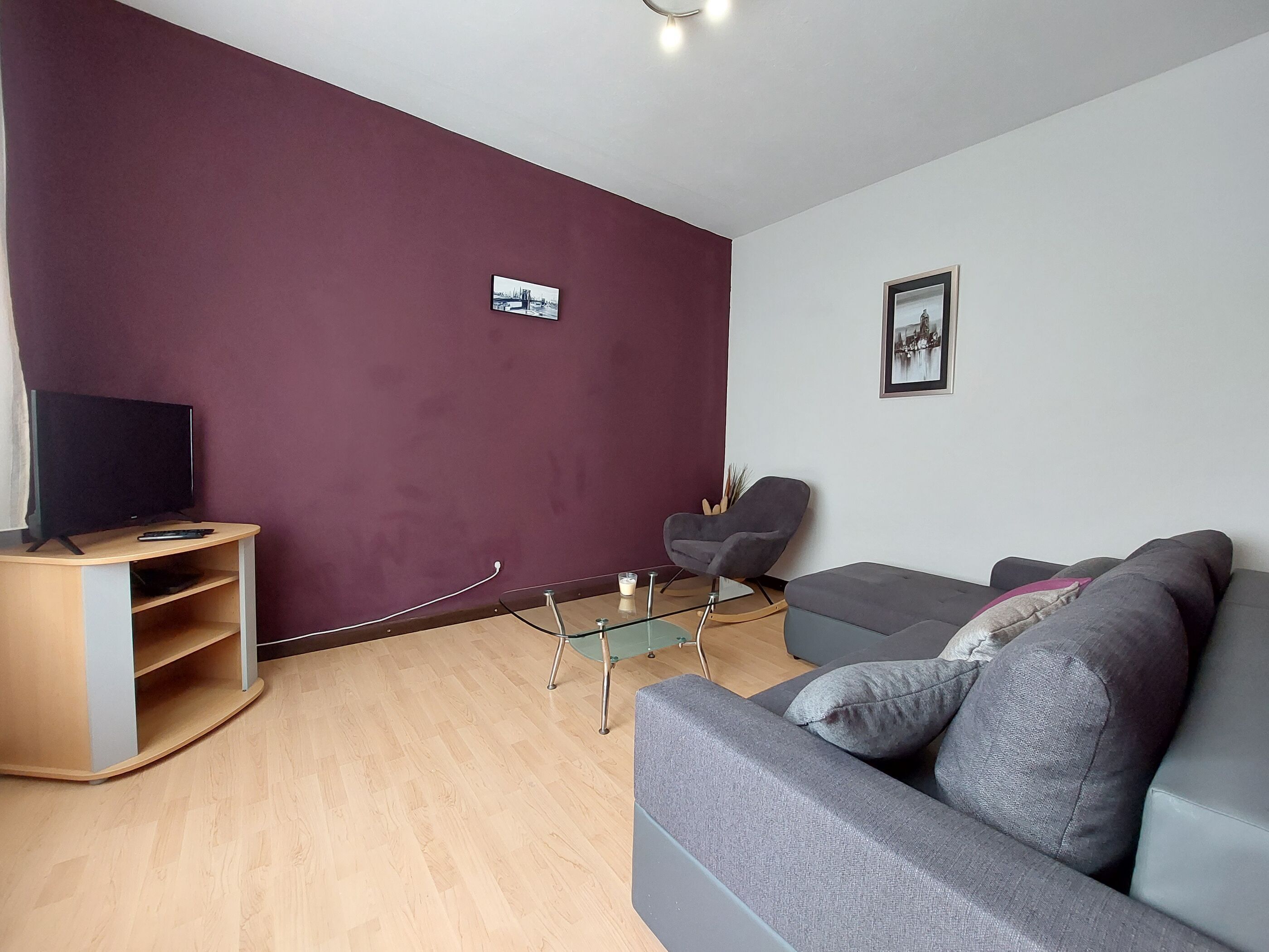 A modern living room with a television on a wooden stand, a grey sofa, and a glass coffee table.