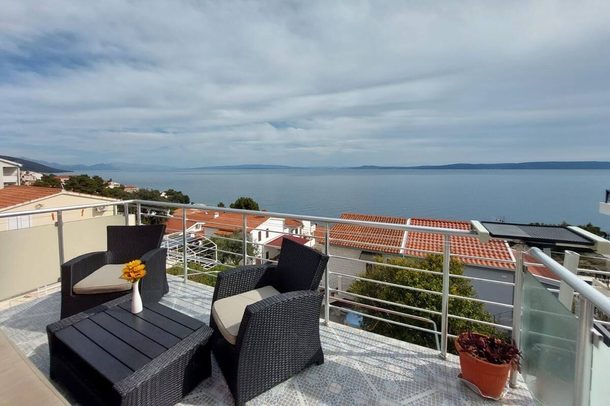 A balcony with wicker furniture, a potted plant, and a view of a body of water and distant land.