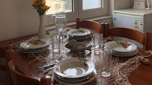A dining table set with plates, glasses, and a vase of flowers, with a view of the sky through a window. - Apartments Mladen (Okrug)