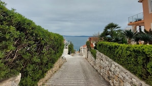A stone staircase leading to a coastal area with a view of the sea, surrounded by lush greenery and traditional architecture. - Apartments Mladen (Okrug)