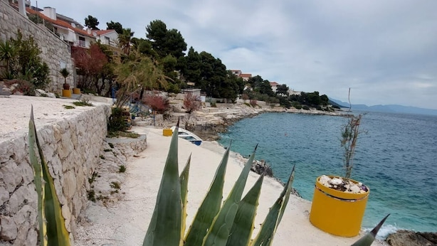 A coastal walkway with a stone wall, yellow planters, and a view of the sea. - Apartments Mladen (Okrug)