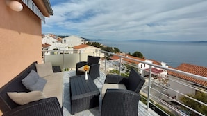 A balcony with wicker furniture, a small table, and a vase with flowers. - Apartments Mladen (Okrug)