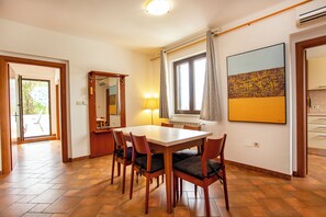 A dining area with a wooden table and chairs, a window with curtains, a mirror, and a painting on the wall. - Apartments Sinisa (Rovinj)