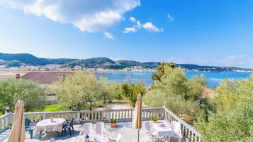 Eine Terrasse mit Sitzgelegenheiten im Freien, mit Blick auf eine Küstenlandschaft mit Hügeln und einem Gewässer.
