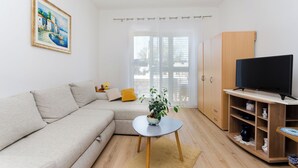 A living room with a sofa, a small table with a plant, a TV stand, and a painting on the wall. - Apartments Zorka (Rab)