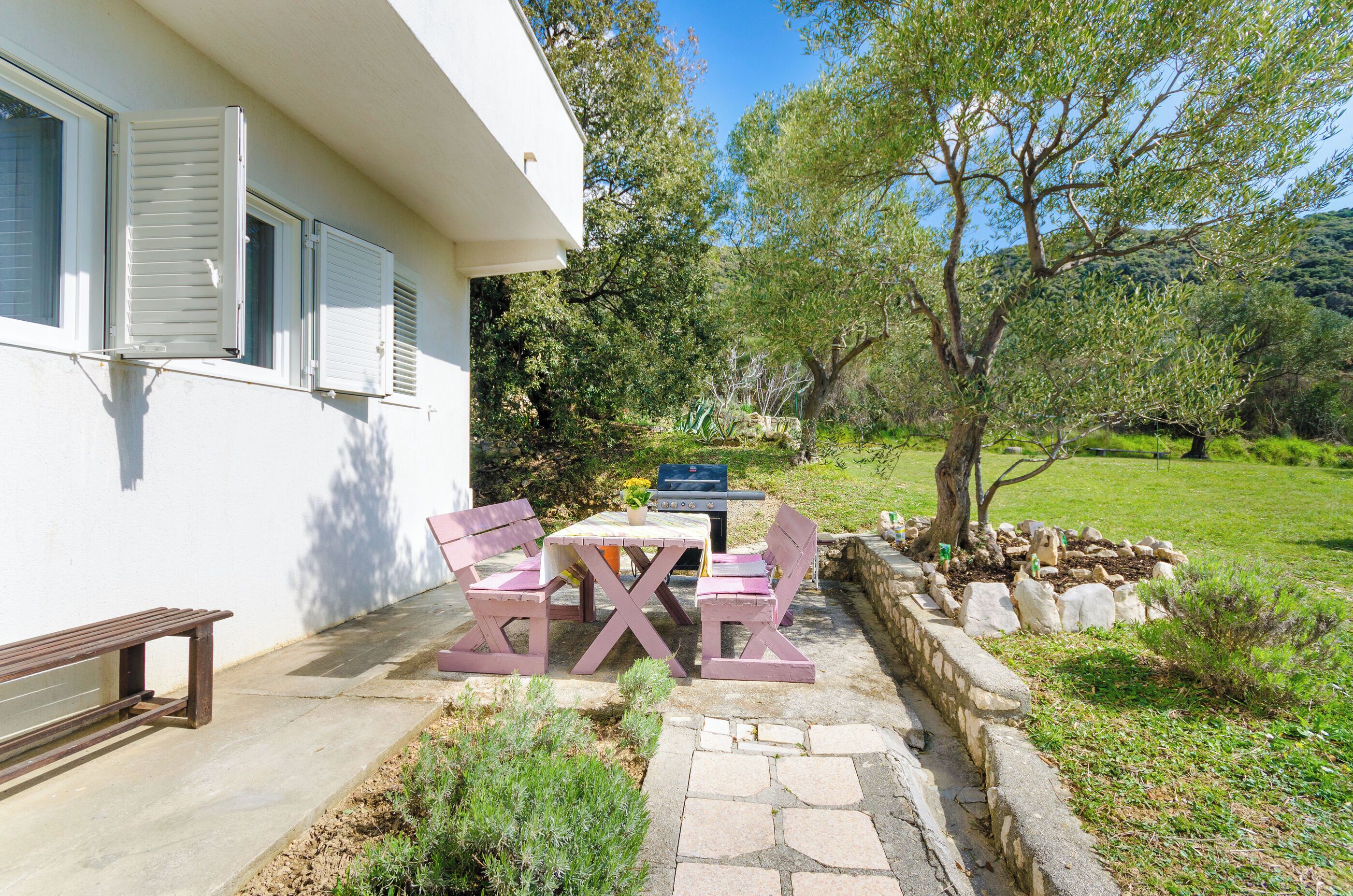 A patio with a table and chairs, a barbecue grill, and a stone pathway leading to a white building with shutters.