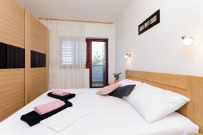Ein ordentlich bezogenes Bett mit weißer und schwarzer Bettwäsche, einem pinkfarbenen und schwarzen Kopfkissen und einem Paar gefalteter Handtücher. Auf dem Nachttisch neben dem Bett steht eine kleine Topfpflanze.