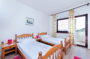 A room with two wooden beds, a nightstand with a red lamp, a window with curtains, and a framed picture on the wall. - Apartments Zorka (Rab)