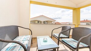 A balcony with wicker furniture and a glass table, overlooking a residential area with houses. - Apartments Anka (Vir)