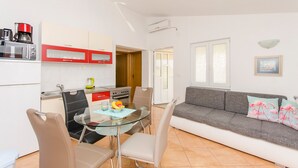 A modern kitchen with white cabinets, a red microwave, and a dining area with a glass table and chairs. - Apartments Anka (Vir)