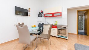 A compact kitchen with a dining area, a TV mounted on the wall, and a microwave. - Apartments Anka (Vir)