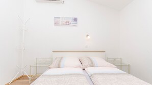 A bedroom with a bed, a wall-mounted air conditioner, a wall art piece, and a bedside lamp. - Apartments Anka (Vir)