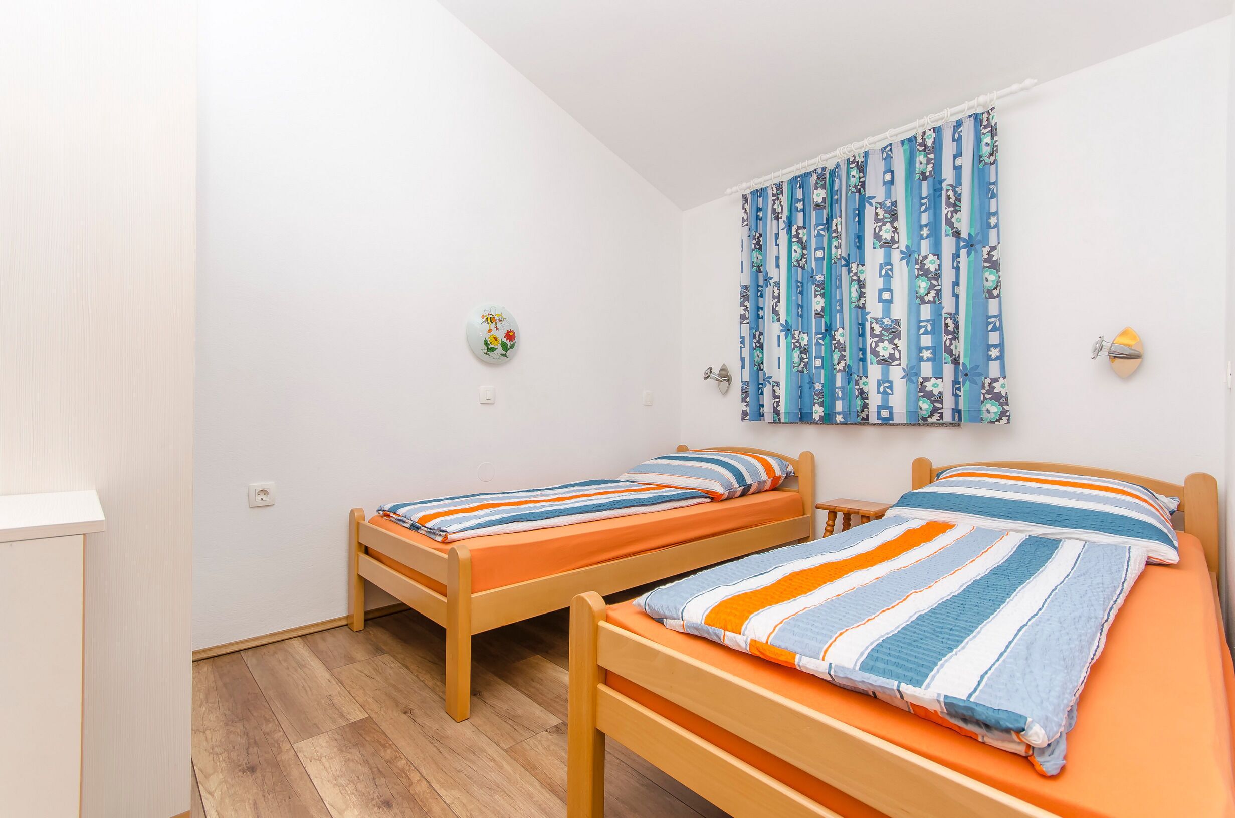 Une chambre avec deux lits en bois, dotés de draps à rayures, un rideau bleu à motifs et un petit élément de décoration murale.