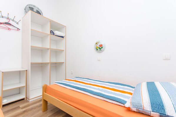 A bedroom with a bed, a wardrobe, a small table, and a wall-mounted fan. - Apartments Anka (Vir)