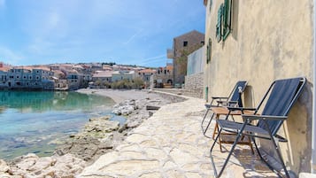 Un paseo marítimo empedrado con mesas al aire libre y vista a un pueblo costero.