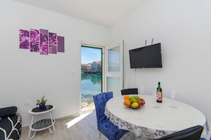 A balcony with a dining table, chairs, a fruit basket, wine glasses, a bottle, and a TV. - Apartment Paradise (Postira)