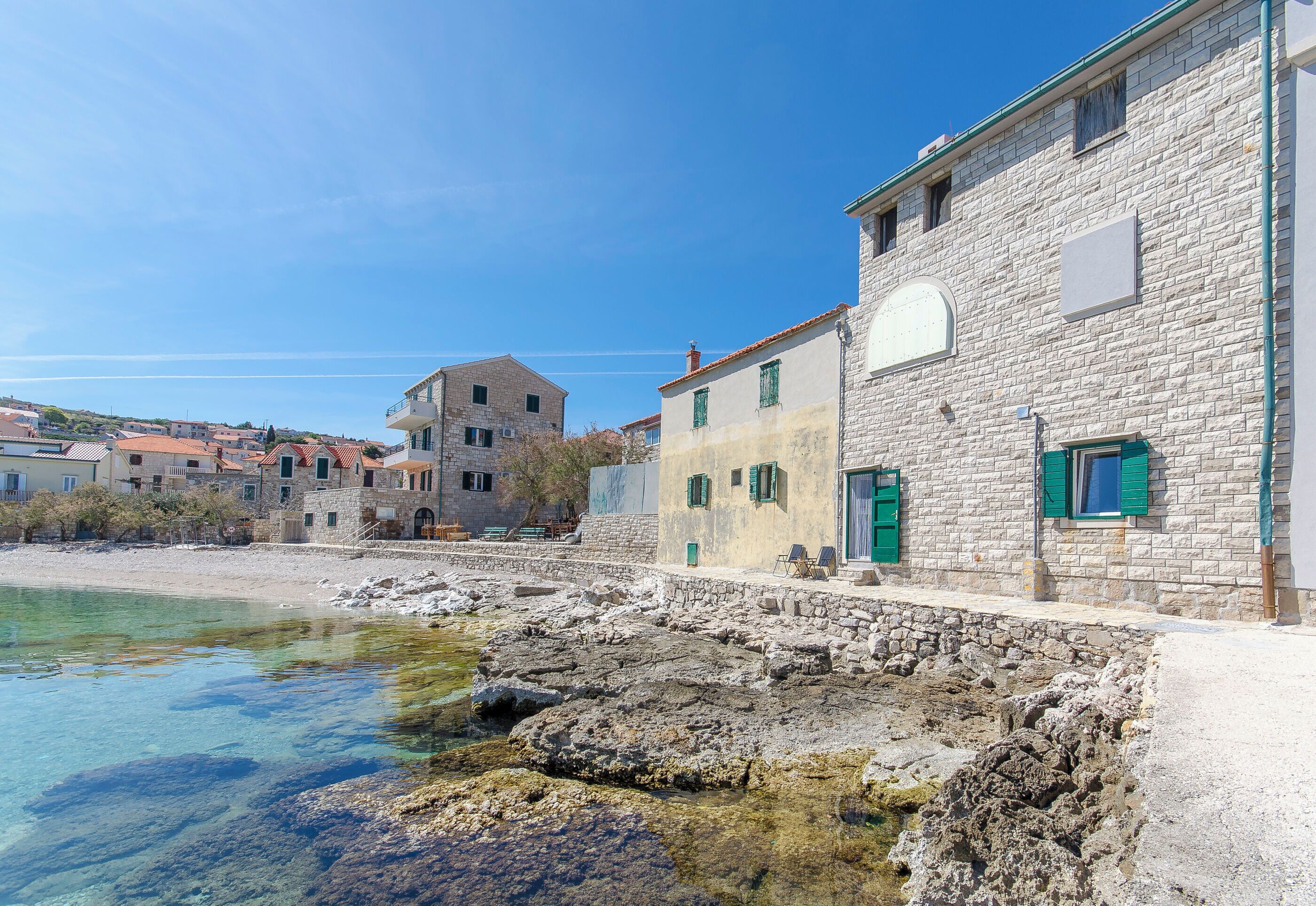 Un edificio costero con paredes de piedra, vista despejada al mar y un balcón.