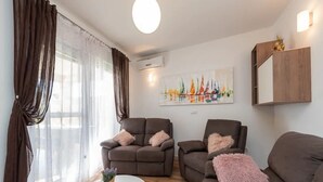 Un salon moderne avec un ensemble de canapés, une table basse ronde et un tableau représentant des voiliers.