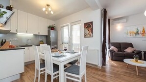 Une cuisine moderne avec des meubles blancs, une table à manger avec des chaises et un coin salon comprenant un canapé et une table basse.