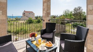 Un balcon agrémenté de meubles en osier, une table avec des éléments pour le petit-déjeuner et une vue sur une maison et la verdure.