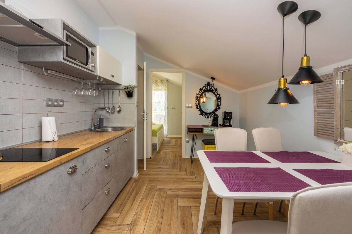 A modern kitchen with a microwave, sink, and wooden countertop. There is a dining area with a table and chairs, and a hallway leading to another room.