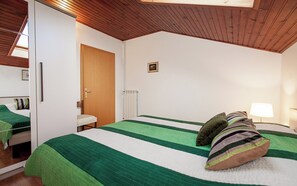 Ein Schlafzimmer mit Holzboden, einem Bett mit grün-weißer Bettwäsche, einer Nachttischlampe und einer Heizung.