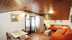 Ein gemütliches Wohnzimmer mit Holzbalkendecke, einem Essbereich mit Tisch und Stühlen sowie einem orangefarbenen Sofa.