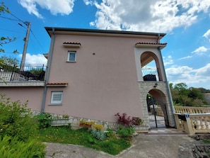 A two-story building with a stone archway entrance, a small balcony, and a gated driveway. - Apartment Sabrina (Crikvenica)