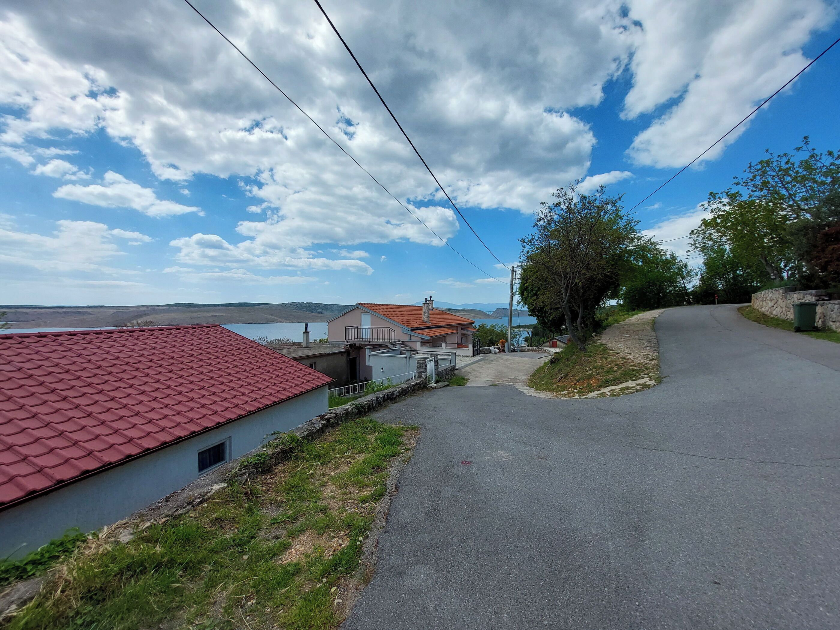 A residential street with houses, a paved road, and a view of a body of water in the distance.