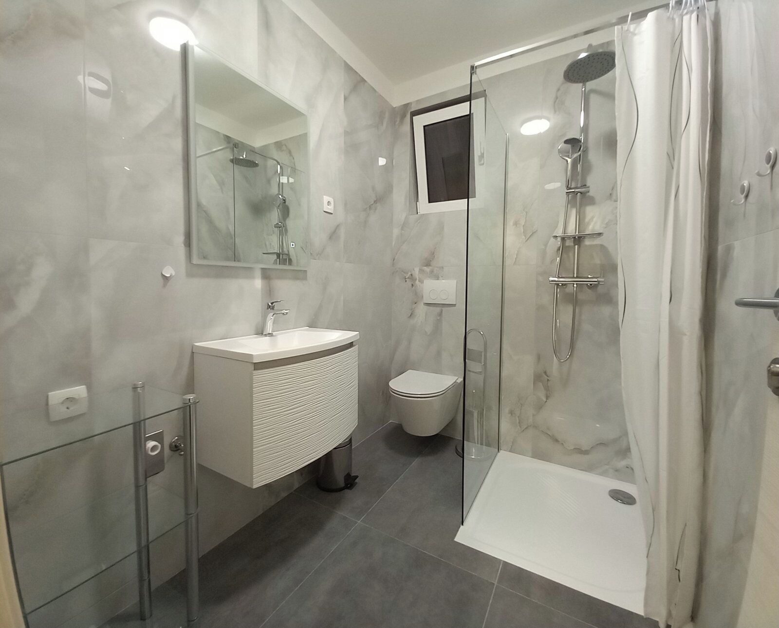 A modern bathroom with a glass-enclosed shower, a white sink, and a toilet.