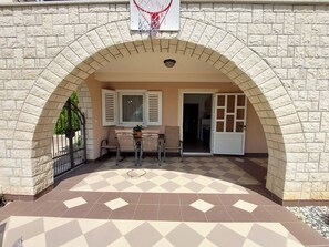 Ein Terrassenbereich im Freien mit Schachbrettmuster-Boden, einem Basketballkorb und einer Sitzgelegenheit.