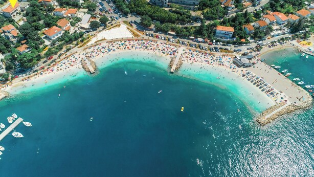 Vista aerea di una cittadina costiera con spiaggia, barche e edifici.