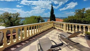 Un balcone con pavimento a scacchi, due poltrone e vista su un lago e delle montagne.