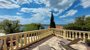 A balcony with a checkered floor, two lounge chairs, and a view of a lake and mountains.