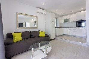 Una sala de estar moderna con un sofá gris, una mesa de centro de vidrio y un espejo grande en la pared.