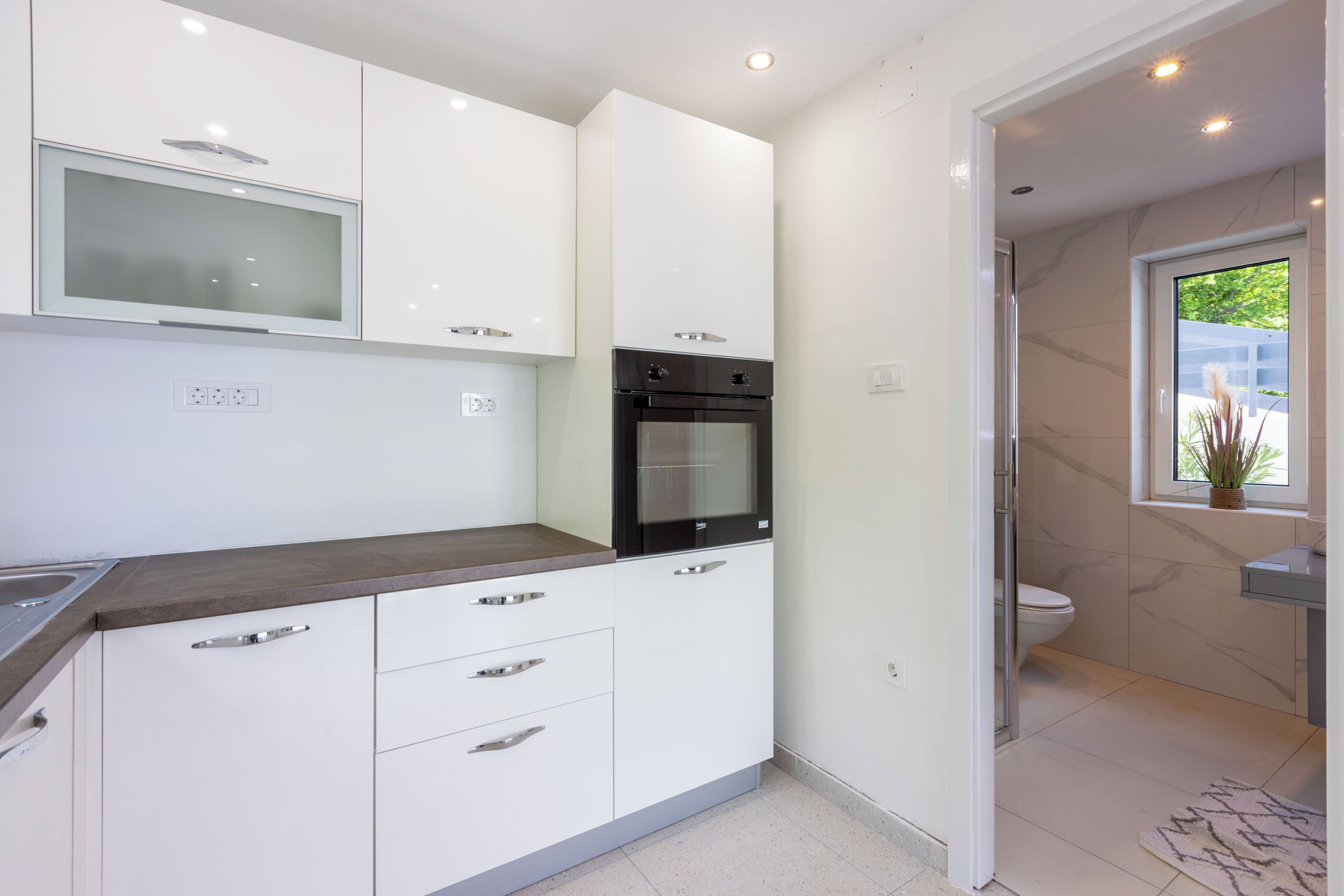 A modern kitchen with white cabinets, a built-in oven, and a microwave.