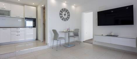 A modern kitchen with white cabinets, a built-in oven, and a dining area with a glass table and chairs.