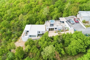 Vista aérea de una casa moderna con piscina, un porche cubierto y un aparcamiento con dos coches.