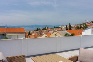 Una terraza en la azotea con vistas a un pueblo costero, que incluye una pared blanca, una mesa de madera y mobiliario de mimbre.