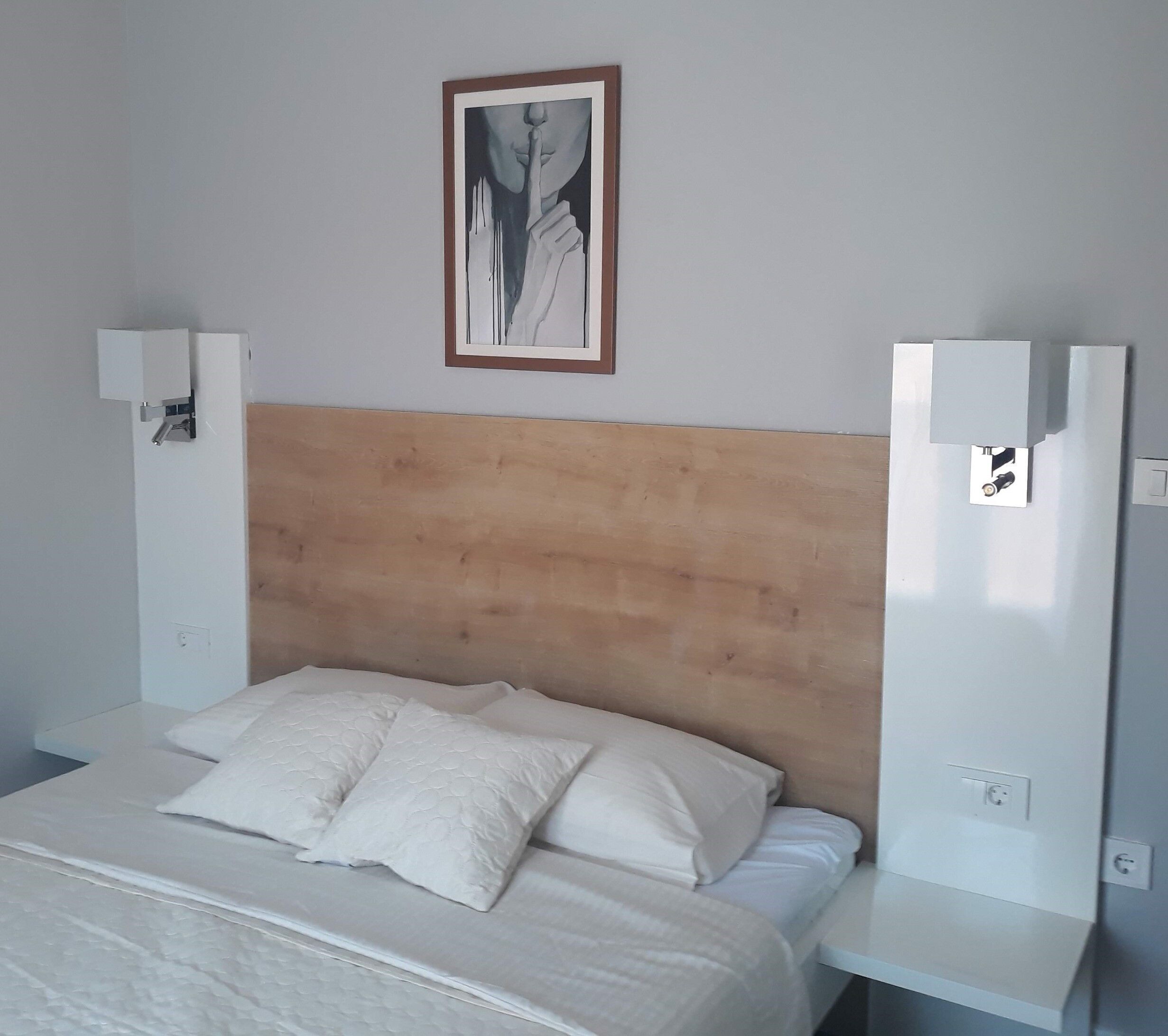 A room with a wooden headboard, a bed with white bedding, and a framed artwork above the bed.