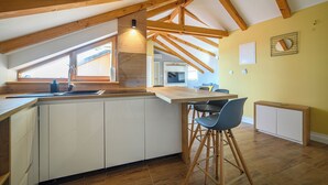 Une cuisine avec des poutres en bois, une grande fenêtre et un coin bar avec des tabourets.
